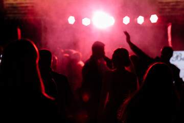 Fototapeta na wymiar cheering crowd in front of bright red stage lights. Silhouette image of people dance in disco night club or concert at a music festival.