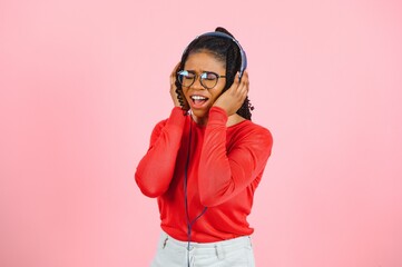 Beautiful woman with afro hair listining to music and dancing on pink background