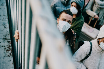 Covid-19 has held humanity hostage. Shot of a group of young people wearing masks while stuck behind a gate in a foreign city.