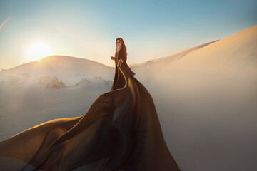 Mystery arabic woman in black long dress stands in desert long train silk fabric fly flytter in...