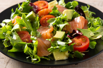 Salmon and avocado salad in plate on wooden table. Close up