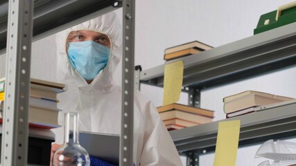 Man scientist or medical working, in protective uniform, looking into the frame in science lab. Close up of male scientist or doctor doing laboratory research and writes results in the journal.