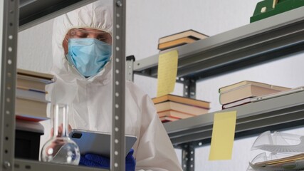 Fototapeta na wymiar Man scientist or medical working, in protective uniform, looking into the frame in science lab. Close up of male scientist or doctor doing laboratory research and writes results in the journal.