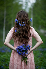 A young girl walks in a field of blue flowers at dusk.