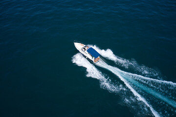 Boat motion top view. Large white boat with people back view on blue water in the rays of the sun aerial view. Boat with a blue tent on the water top view.