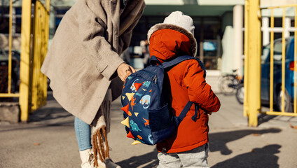 A mother adjusting little son's schoolbag at the kindergarten entrance. - obrazy, fototapety, plakaty