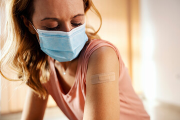 A woman with mask in hospital showing her shoulder after covid 19 vaccination. Vaccination, inoculation and health care. - obrazy, fototapety, plakaty