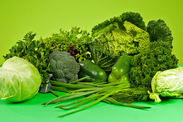 Cabbage, pepper, parsley, dill, onion, lettuce, broccoli on a green background. Assorted vegetables in a pile.