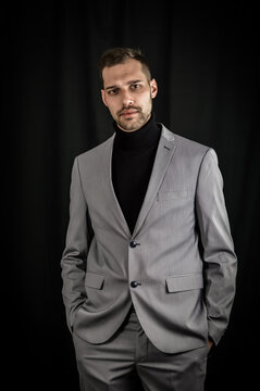portrait of a young businessman in a gray suit and black turtleneck, looking serious with his hands in his pockets