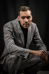 portrait of a young man in a gray suit and a black turtleneck, crouched on the ground looking intently