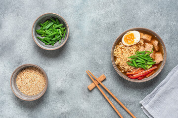 Asian ramen noodle soup with chicken, vegetables and eggs. Gray rustic concrete background. Top view. Japanese food.
