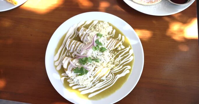 Plate of delicious green Mexican enchiladas on brown table