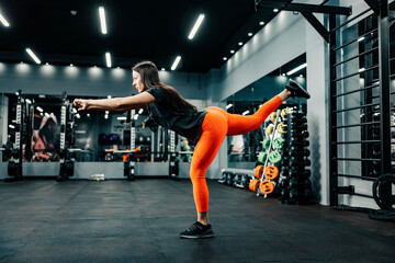 A sporty woman does single leg balance in gym.