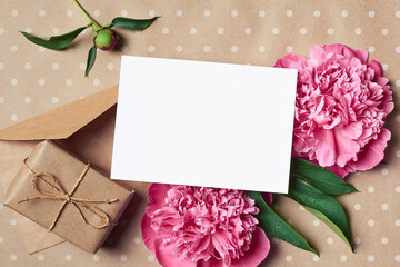Greeting or invitation card mockup with envelope, gift and pink peony flowers on craft paper background
