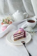 Homemade purple cake with souffle cream and blueberry and cup of tea on the table