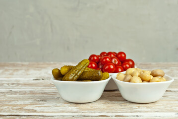 Marinated tomatoes, cucumbers and mushrooms in a white bowl. Snacks with pickled vegetables on a white background. Food on a shabby table. Bowl on an old wooden board.