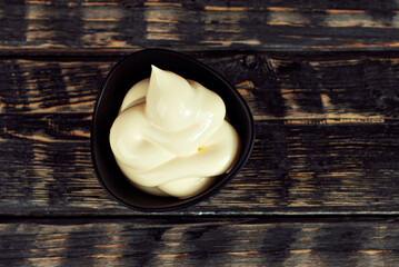 Mayonnaise in a black bowl. Homemade mayonnaise on a black old table. Black bowl with sauce on a background of dark wooden boards.