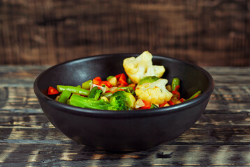 Mix of vegetables close up. Salad of various chopped vegetables. Roasted cabbage, carrots, broccoli, peas in a black plate. Food on the background of an old wooden board.