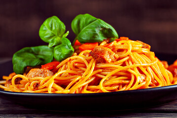 Noodles with carrots and meat in a black plate. Food on a black Yerevan table. Pasta on a background of stale shabby boards.