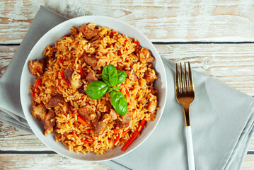 Pilaf in a white plate on a light background. Rice with basil on an old wooden board. Food on shabby wooden table. Top view.