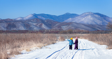 Children in the field are standing on a snowy road and looking at the mountains