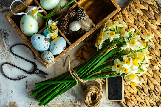 Overhead view of narcissus flowers on a weathered table next to a box of painted Easter eggs