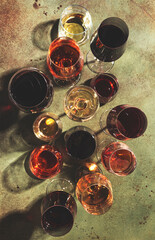 Red, white and rose wines in assortment in glasses on green background, top view. Wine bar, shop, winery, wine tasting concept. Hard light