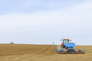 Fototapeta premium A tractor sows cereal crops with a precision seeder in the field.