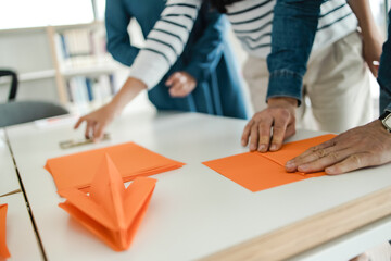 Hands of a man in a denim shirt making the paper plane of orange paper at a business training 