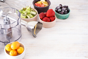 Hand blender and accessories with sliced fruit on a wooden background, place for text.