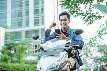 Excited asian man using a cellphone while riding a motorcycle