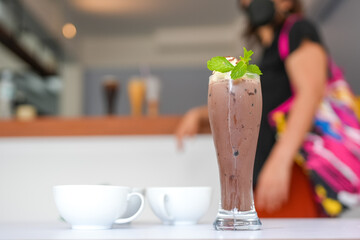 Glass chocolate iced with whip cream on white table.