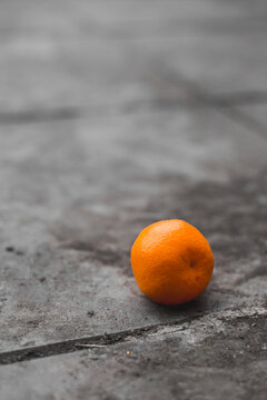 One tangerine fell to the ground from the counter - the season of juicy fruits with vitamins - orange on a gray bright spot