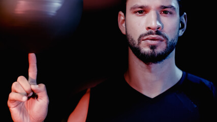 serious sportsman spinning basketball on finger isolated on black