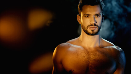 Fototapeta premium bearded and muscular sportsman looking away near smoke on black