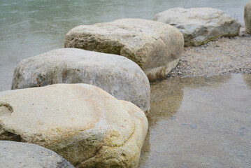 Large round bare pebbles line up forming a path in the frozen water lightly covered with snow in winter