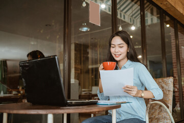Fototapeta na wymiar Asian woman holding coffee cup reading work paper