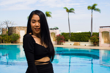 A smiling woman in black dress standing near swimming pool