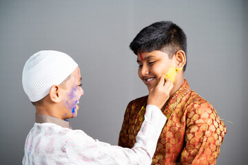 Multiethnic religious kids celebrating holi by applying colors to face on gray background - concept...