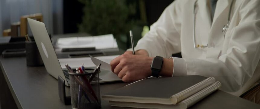 Unrecognizable Caucasian doctor working at his desk late in the evening. Shot with 2x anamorphic lens
