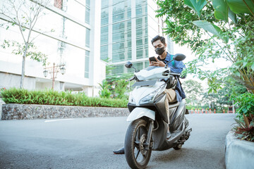 Young man with mask using a cellphone on a motorcycle