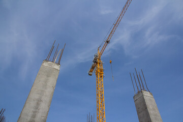 Reinforcement concrete column under construction at the construction site and tower crane against blue sky.