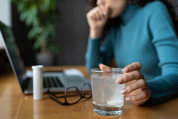 Closeup of painkiller aspirin dissolving in glass of water. Sick businesswoman taking medical pill at office workplace, suffering from migraine headache, feeling bad addicted to antidepressant tablets