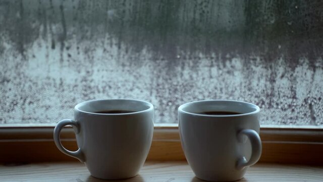 Two cups of hot drink coffee near window, water condensation on window glass, early morning, wake up concept.