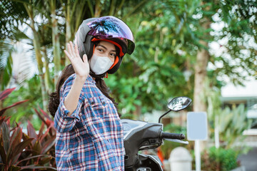 Naklejka premium Asian woman wearing helmet and mask waving while stopping riding