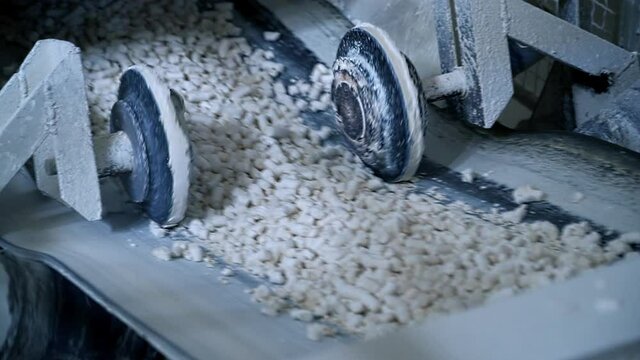 Two wheels moving along both sides of conveyor belt. Line transporting pressed kaolin clay. Close up.