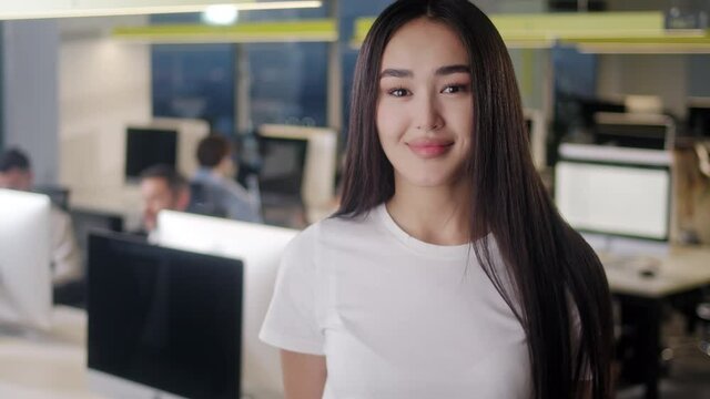 Portrait of Beautiful Asian Woman Wearing White T-Shirt Looking Up to the Camera and Smiling Charmingly. Successful Female Working in Open Space Office