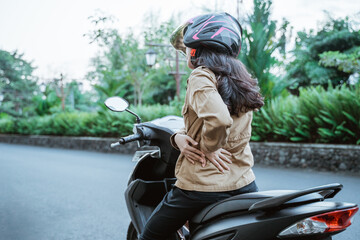 Woman wearing helmet stops riding motorbike due to back pain