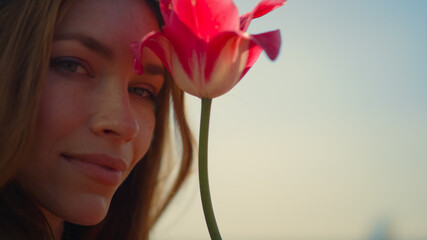 Closeup beautiful woman face enjoying tulip flower in soft sunset light outdoor.