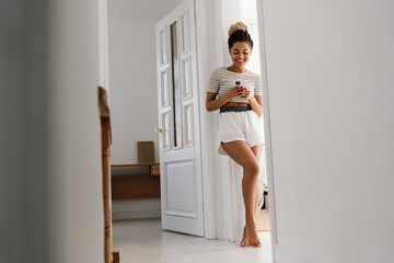 Young black woman smiling and using cellphone at home